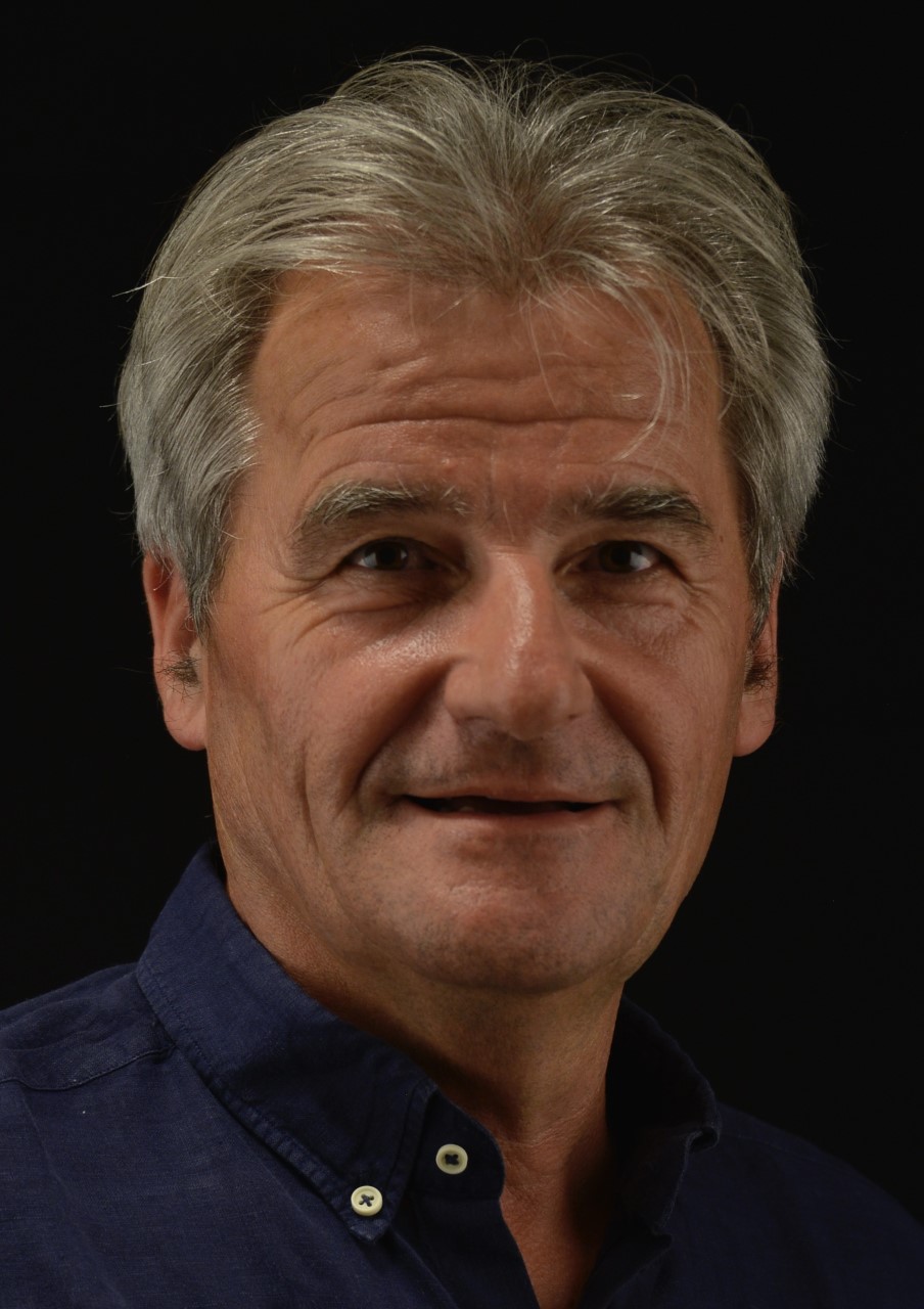 Professional photograph of Professor Philippe Gaud smiling in a shirt, with a black background
